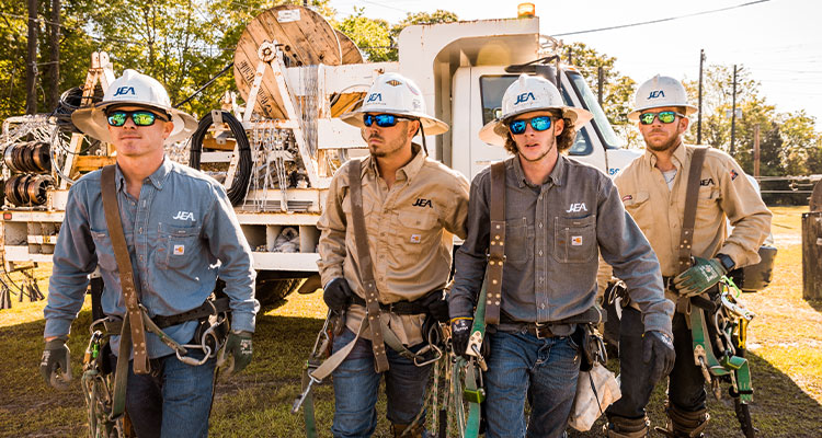 JEA workers in white hard hats with climbing gear