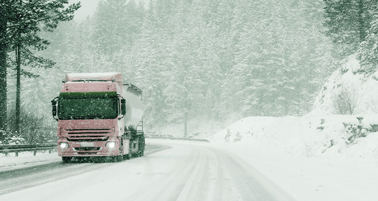 Pink lorry driving through falling snow on a snow covered road