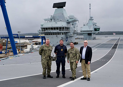 Rear Adm. Peter Stamatopoulos (second from right), Naval Supply Systems Command (NAVSUP) commander, Kurt Wendelken (right), NAVSUP vice commander, Rear Adm. Patrick S. Hayden (left), Logistics, Ordnance and Engineering director, U.S. Naval Forces Europe-Africa (N4) and Captain Richard Hewitt OBE Royal Navy aboard HMS Prince of Wales Oct. 18, 2022. Hewitt, the ship's commanding officer, hosted Hayden and the NAVSUP leaders for a tour of the Queen Elizabeth-class aircraft carrier after they met with various U.K. Ministry of Defense officials at Defense Munitions Crombie, Scotland, U.K. Specific safety boots were provided for participants going aboard HMS Prince of Wales. (U.K. Royal Navy photo by Lt. Cmdr. Stephen Currie/released)