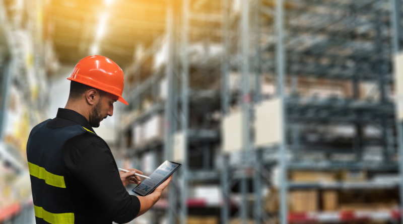 A worker using supply chain management software on a tablet in a warehouse.