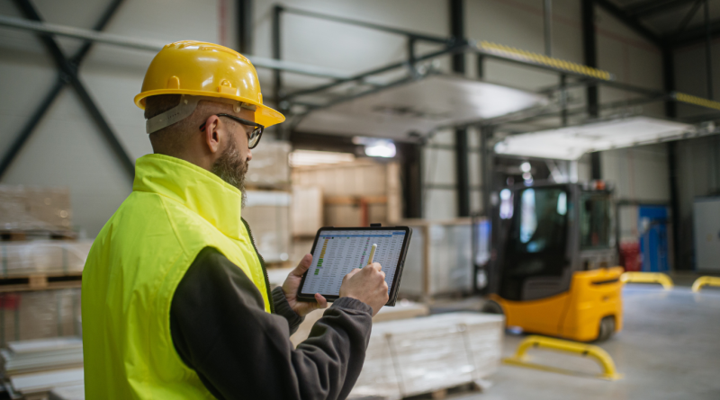 A warehouse worker uses a tablet to manage inventory, illustrating real-time supply chain visibility.