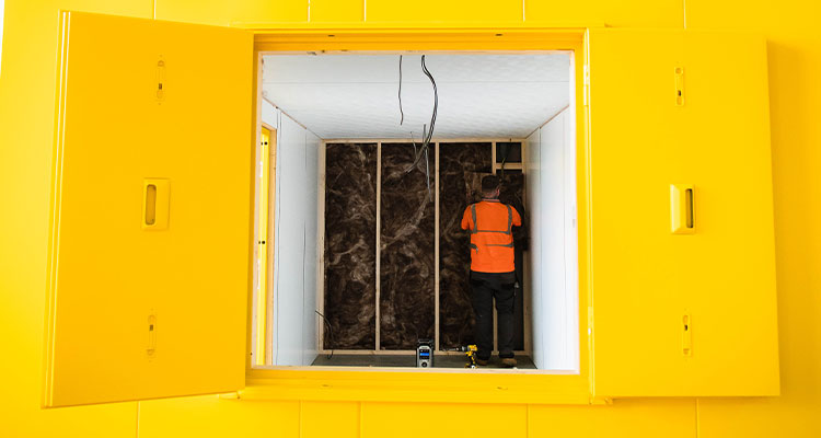 a construction worker installing insulation inside a confined space with a bright yellow exterior and frame.