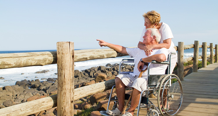 an elderly couple on a wooden boardwalk overlooking a rocky coastline and the ocean.