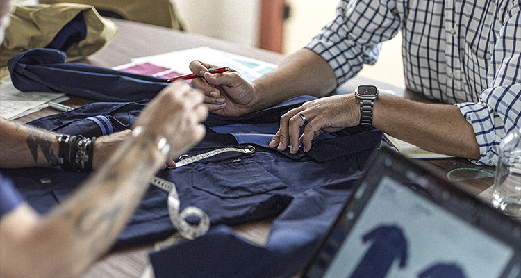 two people working together at a wooden table, likely in a design or tailoring setting.
