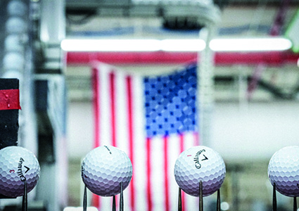 several golf balls positioned on thin metal prongs along an automated assembly line