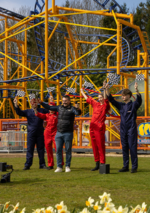 a celebration or promotional event taking place in front of a prominent yellow and blue roller coaster