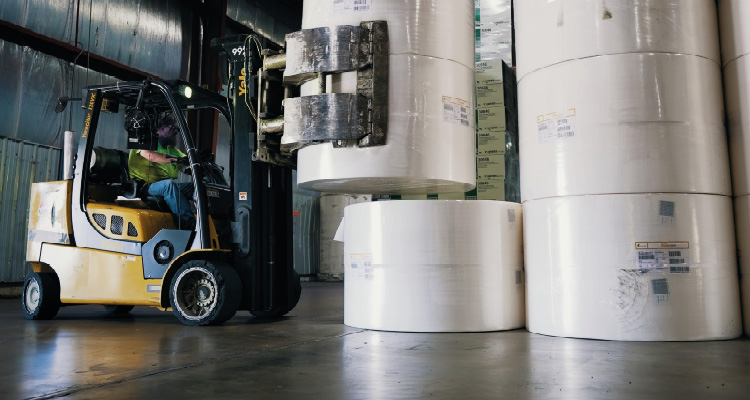 From a single warehouse, WSI evolved into one of the largest, private third-party logistics companies in the US a yellow Yale forklift in an industrial warehouse setting, operated by a person in a lime-green safety shirt