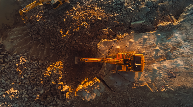 Aerial Drone Shot Directly Above Industrial Excavator Digging Up Rocks On Construction Site On Sunny Day.