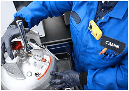 a technician in a blue work uniform using a wrench to connect a hose to a recovery cylinder for handling refrigerant gas