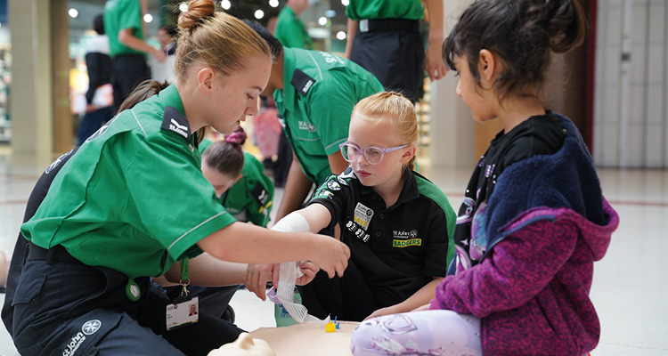 St John Ambulance volunteers demonstrating basic first aid and bandage techniques to children